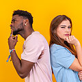 Two multi-ethnic young friends standing back-to-back hesitating