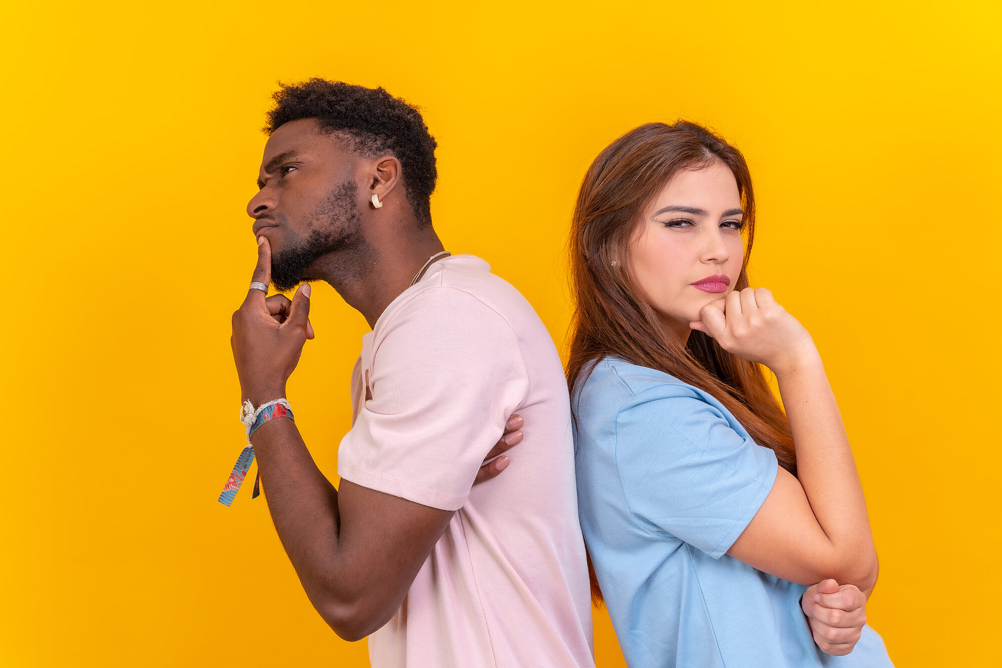 Two multi-ethnic young friends standing back-to-back hesitating