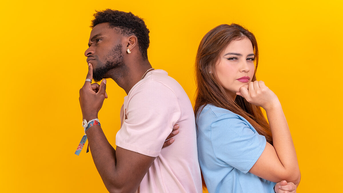 Two multi-ethnic young friends standing back-to-back hesitating