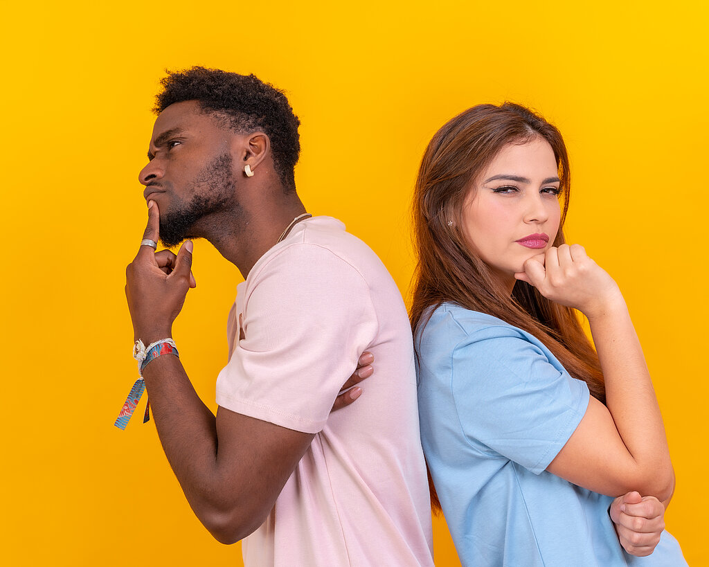 Two multi-ethnic young friends standing back-to-back hesitating