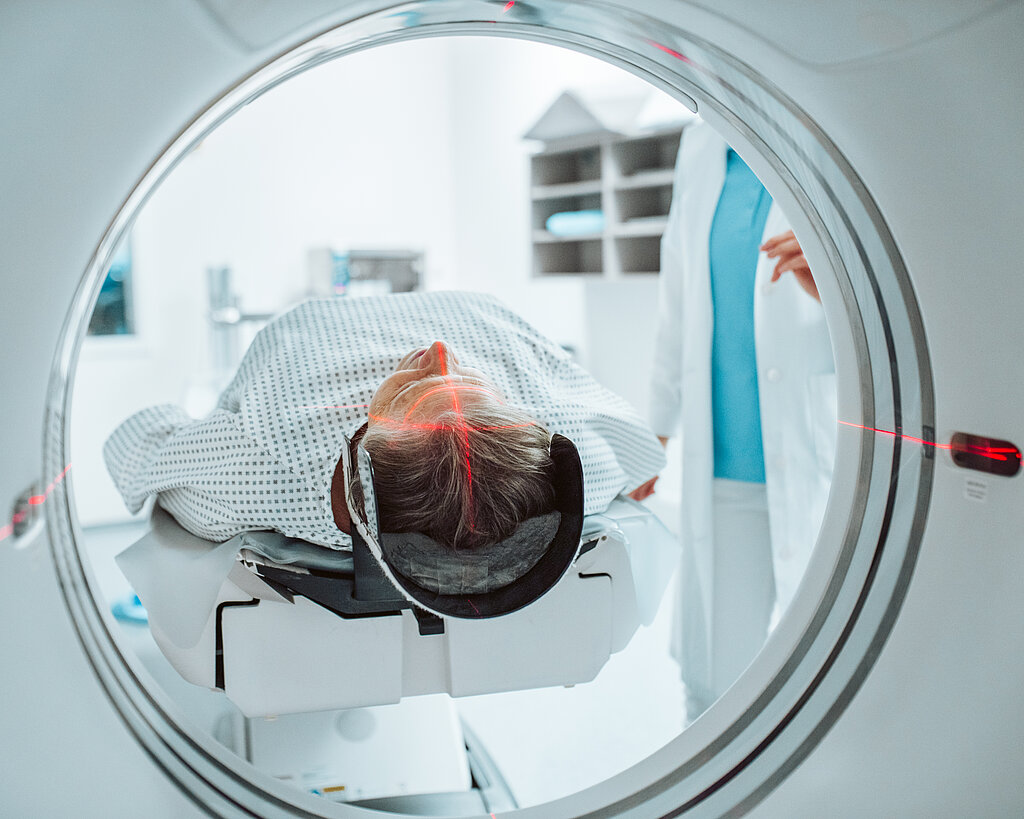 Senior woman positioned for head scan with laser alignment in CT scanner.