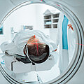 Senior woman positioned for head scan with laser alignment in CT scanner.