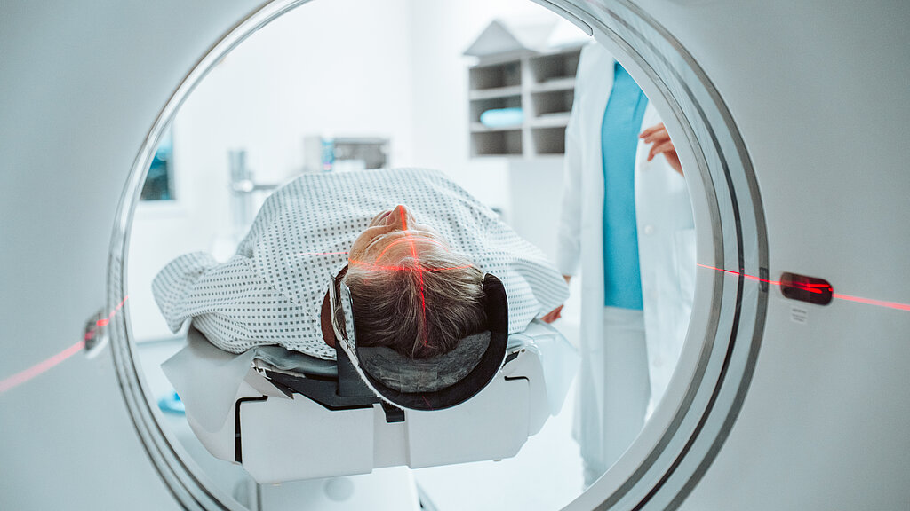Senior woman positioned for head scan with laser alignment in CT scanner.
