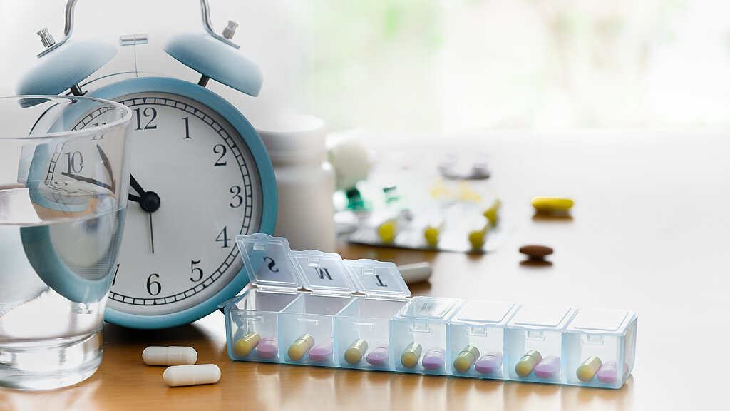 Pill box organiser of vitamins and medicines with alarm clock on the table.