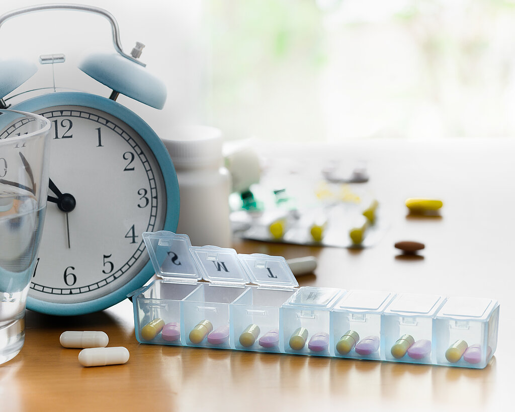 Pill box organiser of vitamins and medicines with alarm clock on the table.