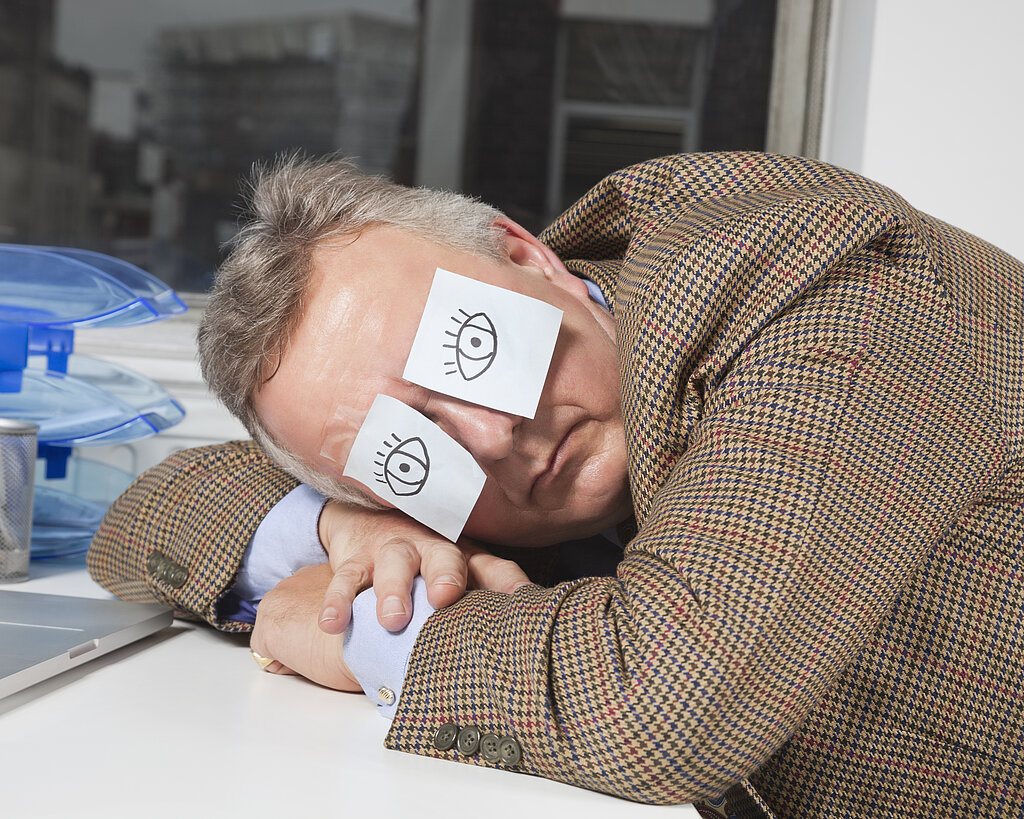 Businessman sleeping with sticky notes on eyes at desk in office