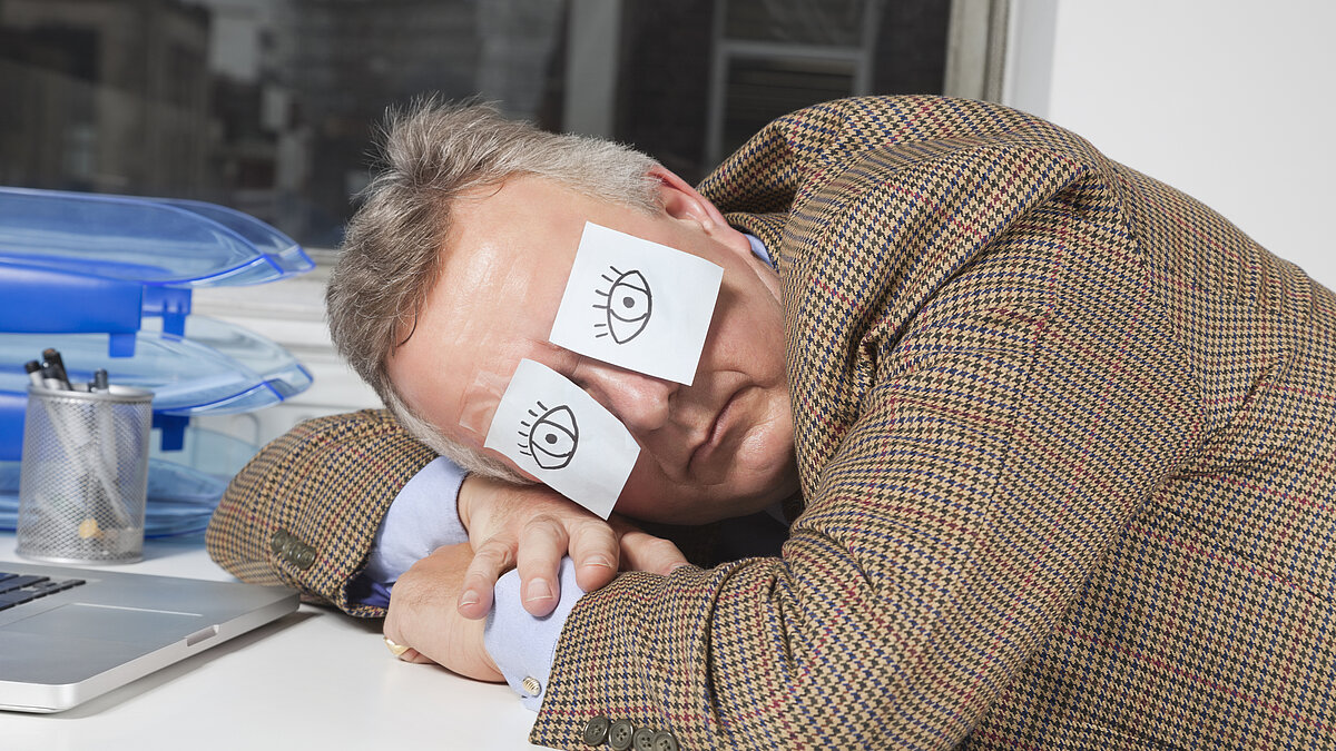Businessman sleeping with sticky notes on eyes at desk in office