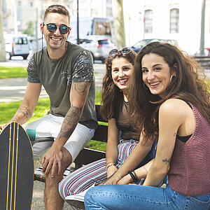 Portrait of three happy friends with skateboard relaxing in an urban park