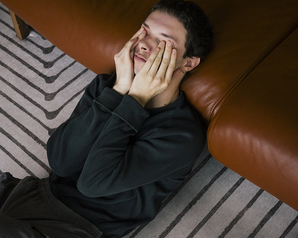 High angle view of man rubbing eyes while reclining on sofa at home