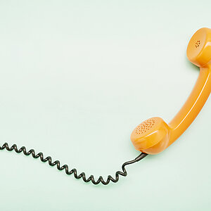 High angle view of an orange old-fashioned telephone receiver on turquoise background