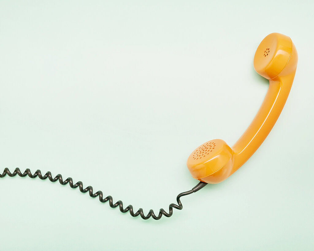 High angle view of an orange old-fashioned telephone receiver on turquoise background